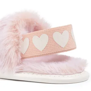 Close-up of pink baby slipper featuring plush faux fur and elastic heart-patterned heel strap