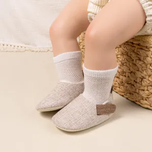 Detail of infant linen walking shoes with velcro strap and white mesh socks on fabric