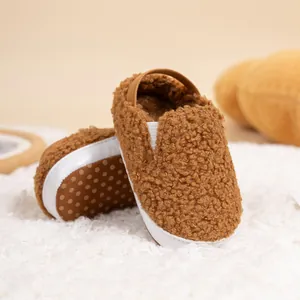 Detail of warm brown teddy fleece baby shoes with anti-slip soles on a soft rug