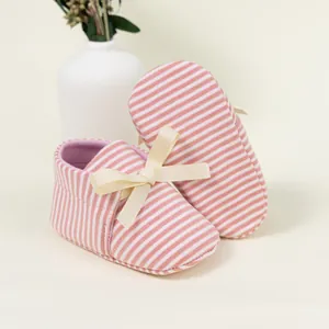 Detailed view of pink striped baby shoes featuring a delicate cream ribbon bow and soft sole