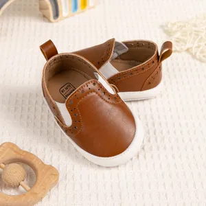 Dettaglio di scarpe primi passi marroni con decori brogue ed elastici bianchi