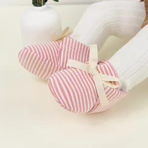 Detail of pink and white striped baby shoes with a beige ribbon bow on a soft cotton surface