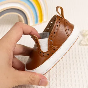 Dettaglio scarpa primi passi in similpelle marrone con motivi brogue e fascia elastica