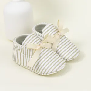 Close-up of baby loafers featuring green striped fabric and beige ribbon bow accents