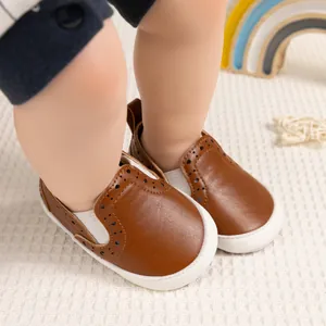 Dettaglio di scarpe primi passi marroni con motivi brogue su tappeto bianco