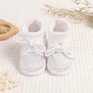 Close-up of white baby shoes with heart embroidery and soft lace on textured background