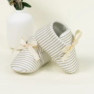 Detail showing baby walking shoes with green and white stripes and a satin bow