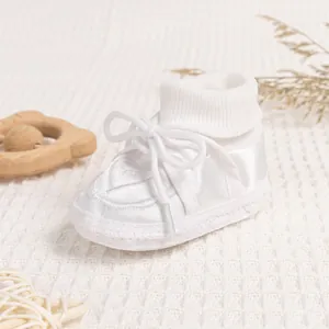 Detailed close-up of white satin baby walking shoes with ribbon bow on knit blanket