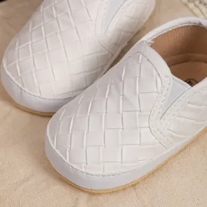 Close-up of white woven slip-on baby shoes with elastic straps on rustic fabric
