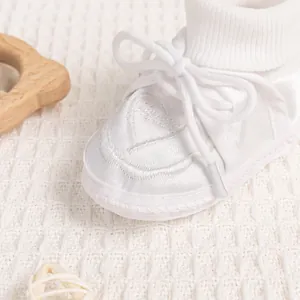 Close-up of white satin baby shoes with heart embroidery and lace details
