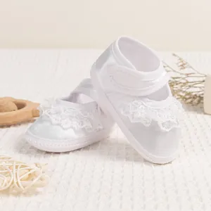Detail of white satin baby shoes featuring elegant lace trim and secure velcro closure