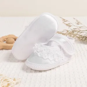 Close-up of white satin baby shoes with lace trim and soft sole for christening