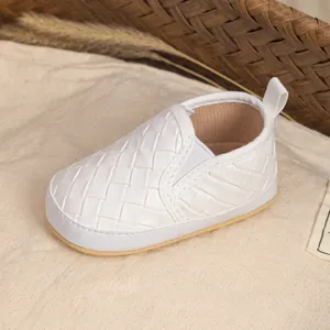 Close-up of white woven slip-on baby shoes with soft non-slip soles on linen