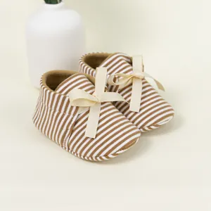 Striped baby walking shoes with bow decoration on a soft neutral background