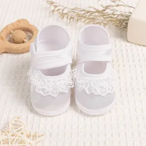 Close-up of white baby lace shoes on waffle blanket with decorative wooden rattle