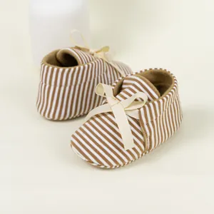 Detail of brown striped baby shoes with a beige ribbon bow and soft cotton fabric