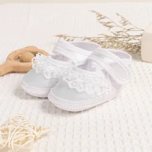 Close-up of white satin baby shoes with elegant lace frills and adjustable velcro strap
