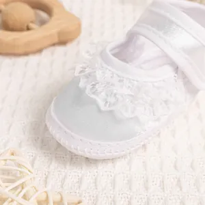 Close-up of white satin baby walking shoes with delicate double-layered lace details