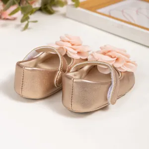 Gros plan de chaussures Mary Jane bébé or rose avec grande fleur en tissu et velcro