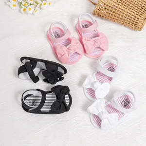 Flat lay of pink, black, and white baby bow sandals with striped insoles on a soft background