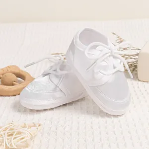 Detailed view of white satin baby walker shoes with lace ribbons and soft soles