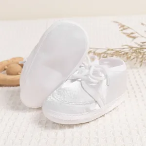 Detail of white satin baby walking shoes with lace ribbon on soft fabric sole
