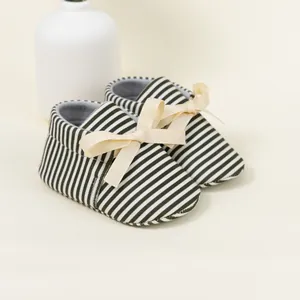 Close-up of striped baby shoes with beige grosgrain ribbon bows on a minimalist background