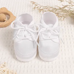 Detailed view of white satin baby baptism shoes with soft soles and lace-up ribbons