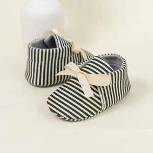 Detail view of baby soft-sole shoes with black and white stripes and a beige ribbon bow