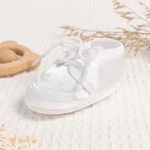Detailed view of white baby walking shoes with lace satin fabric on soft fabric background