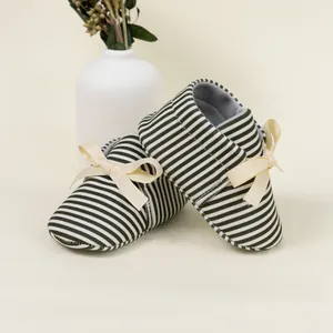 Detail of baby stripe shoes with cream ribbon bow on a cozy beige background