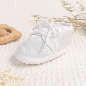 Detailed side view of white satin baby walking shoes with lace bow on knit background