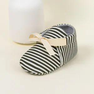 Detail of striped baby shoes with a beige bow on a soft fabric upper