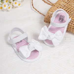 Detail of white infant sandals with lace bow, velcro strap, and striped fabric insole
