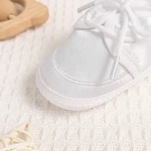 Detailed close-up of white satin baby walking shoes with delicate lace and soft soles
