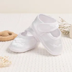 Detail view of white satin baby shoes featuring heart embroidery and velcro straps