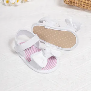Detail of white baby sandal featuring large bow, striped insole and non-slip sole
