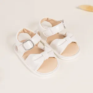 White baby sandals with cute bow and adjustable straps on a soft beige background