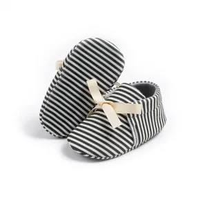 Close-up of soft cotton baby shoes with black and white stripes and a beige ribbon bow