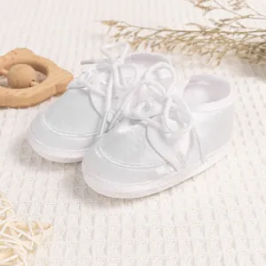 Detail of white satin baby baptism shoes with soft soles and ribbon laces on a waffle cloth