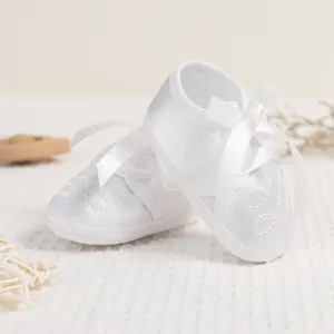 Detailed view of white satin baby baptism shoes with embroidery and silk ribbon ties