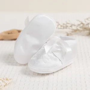 Detail of white satin baby shoes with ribbon bow and embroidery on soft waffle fabric