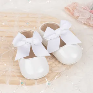 Detailed shot of white baby Mary Jane shoes with large bows on a lace background