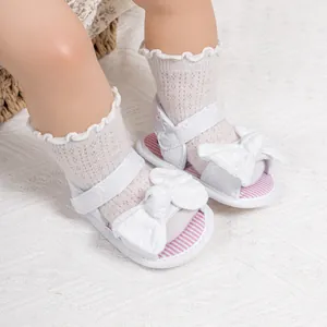 Detail of white baby bow sandals with striped insoles and lace socks on textured carpet
