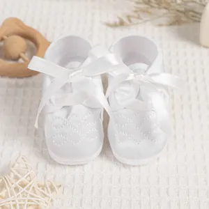 Detail of white satin baby shoes with diamond embroidery and silk bow on knit blanket