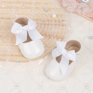 Top view of white baby princess shoes with large bow details on a rustic wooden tray
