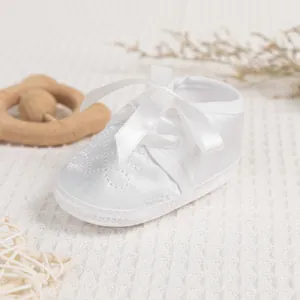 Macro detail of baby christening shoe with satin fabric, cross embroidery and silk bow