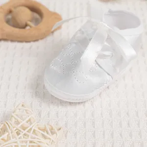 Detail of white satin baby baptism shoe with quilted stitching on a soft knit blanket
