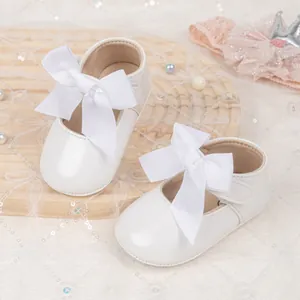 Detail of white Mary Jane baby shoes with large bow on a decorative wooden tray
