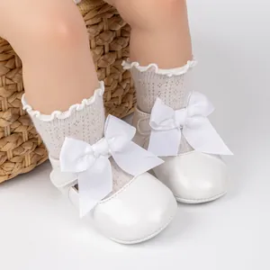 Detail view of white Mary Jane baby shoes with large bow and lace socks in a woven basket